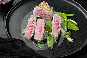 Fried tuna steak in sesame with spring onions and sugar snap peas , on plate, on black stone background