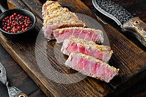 Fried tuna steak in sesame, on wooden serving board, on old dark  wooden table background