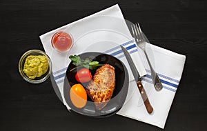 Fried  turkey steak on a black plate with tomatoes