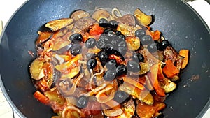 Fried vegetables: onions, carrots, peppers, decorated with black olives. Vegetable stew in a pan. The process of stewing vegetable