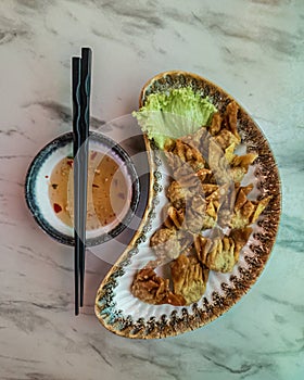 Fried wantan served on the plate together with the dipping sauce and a pair of chopsticks. Top view photo