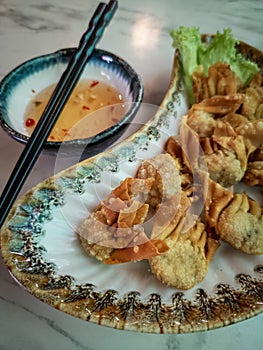 Fried wantan served on the plate together with the dipping sauce and a pair of chopsticks. Top view photo