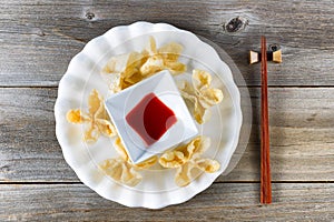 Fried wanton shells and sweet dipping sauce in white bowl on rustic wood