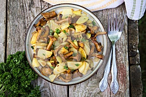 Fried young potatoes with chanterelles mushrooms in bowl on old