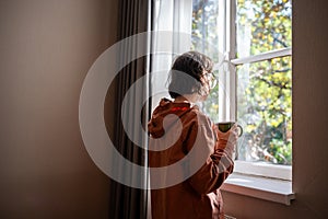 Friendless teen girl standing near window, dreaming of walking in street in warm sunny weather photo