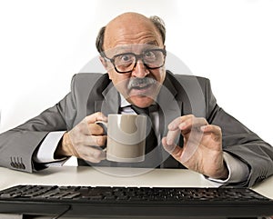 friendly 60s bald senior business man holding coffee cup drinking happy having breakfast at office computer desk smiling