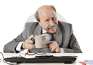 friendly 60s bald senior business man holding coffee cup drinking happy having breakfast at office computer desk smiling