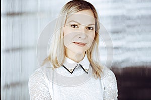 Friendly adult business woman standing straight. Business headshot or portrait in sunny office