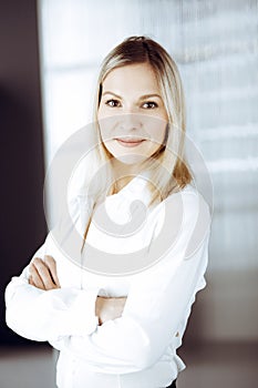 Friendly adult business woman standing straight. Business headshot or portrait in sunny office