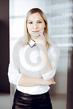 Friendly adult business woman standing straight. Business headshot or portrait in sunny office