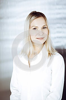 Friendly adult business woman standing straight. Business headshot or portrait in sunny office