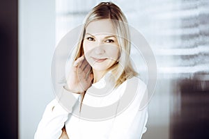 Friendly adult business woman standing straight. Business headshot or portrait in sunny office