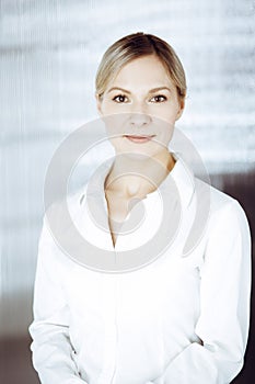 Friendly adult business woman standing straight. Business headshot or portrait in sunny office