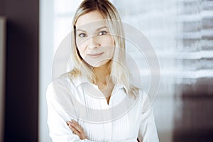 Friendly adult business woman standing straight. Business headshot or portrait in sunny office