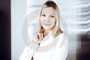 Friendly adult business woman standing straight. Business headshot or portrait in sunny office