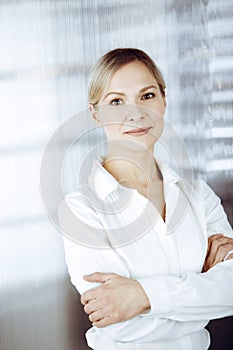 Friendly adult business woman standing straight. Business headshot or portrait in sunny office