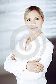 Friendly adult business woman standing straight. Business headshot or portrait in sunny office