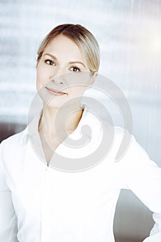 Friendly adult business woman standing straight. Business headshot or portrait in sunny office