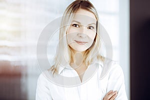 Friendly adult business woman standing straight. Business headshot or portrait in sunny office