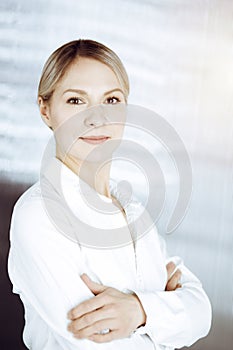 Friendly adult business woman standing straight. Business headshot or portrait in sunny office