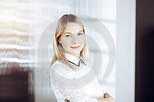 Friendly adult business woman standing straight. Business headshot or portrait in sunny office