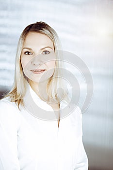 Friendly adult business woman standing straight. Business headshot or portrait in sunny office