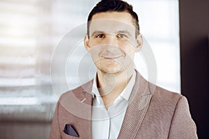 Friendly adult businessman in grey jacket. Business headshot or portrait in sunny office