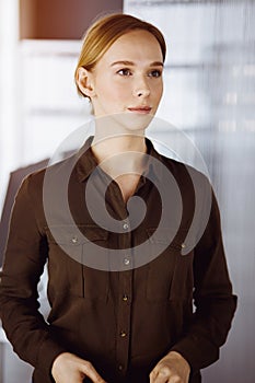 Friendly adult casual dressed business woman standing straight. Concept of a business headshot or portrait in office