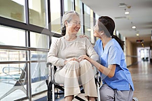 Friendly asian caregiver talking to senior resident in nursing home