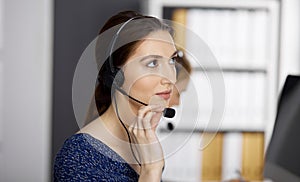 Friendly asian or Latin american businesswoman talking by headset in office. Call center and diverse people group in