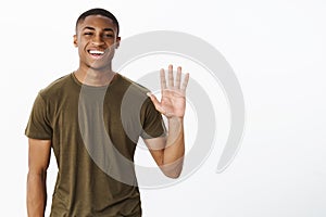 Friendly attractive nice african american male friend raising palm to wave smiling broadly saying hello, greeting