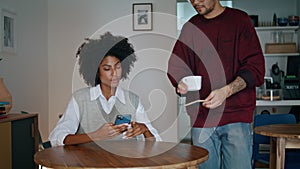 Barista bringing cup coffee to african american woman client. Girl sitting table photo