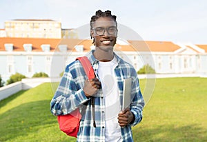 Friendly black student guy with backpack holding closed laptop outside