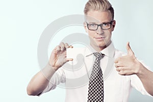 Friendly businessman giving thumbs up at white empty card.