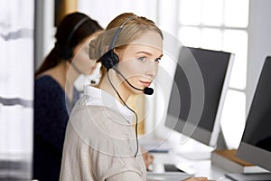 Friendly businesswoman talking by headset in office. Call center and diverse people group in business