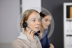 Friendly businesswoman talking by headset in office. Call center and diverse people group in business