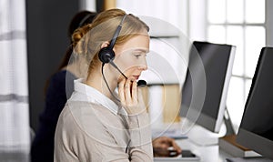 Friendly businesswoman talking by headset in office. Call center and diverse people group in business