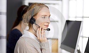 Friendly businesswoman talking by headset in office. Call center and diverse people group in business