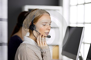 Friendly businesswoman talking by headset in office. Call center and diverse people group in business