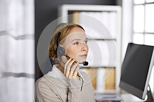 Friendly businesswoman talking by headset in office. Call center and diverse people group in business