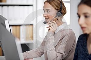 Friendly businesswoman talking by headset in office. Call center and diverse people group in business