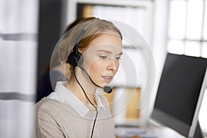 Friendly businesswoman talking by headset in office. Call center and diverse people group in business