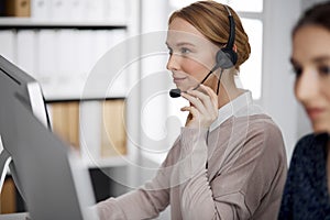 Friendly businesswoman talking by headset in office. Call center and diverse people group in business