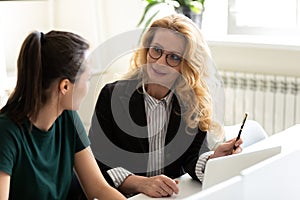 Friendly capable mature businesswoman training younger colleague intern