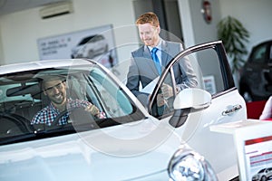 Friendly car dealer showing new car to customer