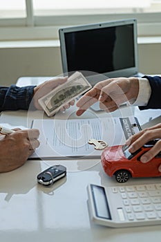 A friendly car salesman is sitting at a table with a customer. and provide the customer with a properly signed purchase