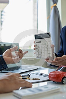 A friendly car salesman is sitting at a table with a customer. and provide the customer with a properly signed purchase