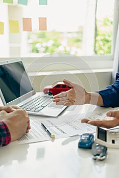 A friendly car salesman is sitting at a table with a customer. and provide the customer with a properly signed purchase