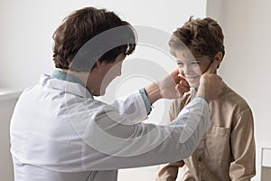 Friendly caring male pediatrician examining kid, touching lymph nodes