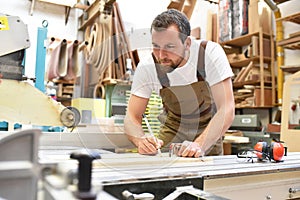 friendly carpenter with ear protectors and working clothes working on a saw in the workshop